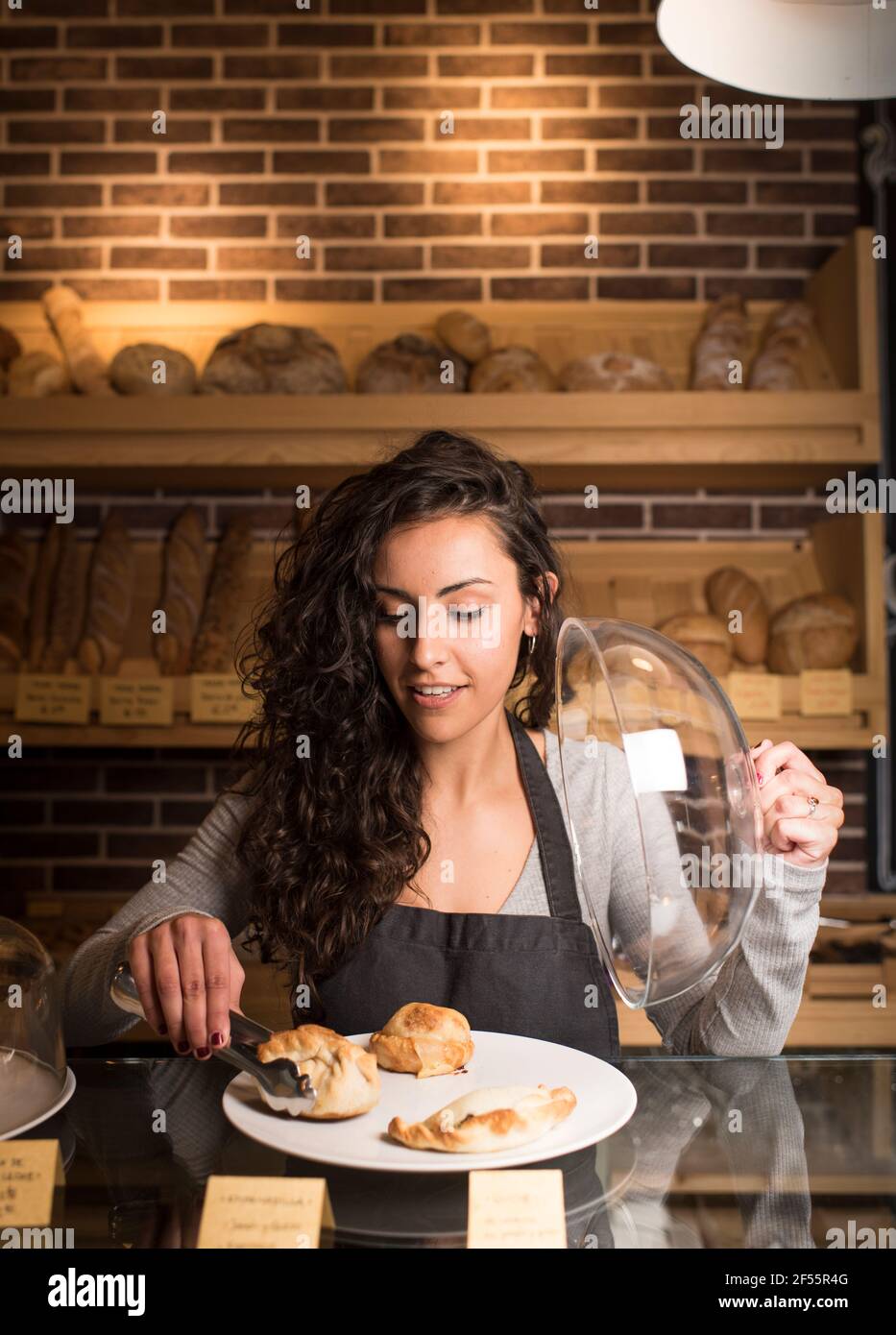Junge Besitzerin, die in der Bäckerei Backwaren auf dem Teller serviert hat Stockfoto