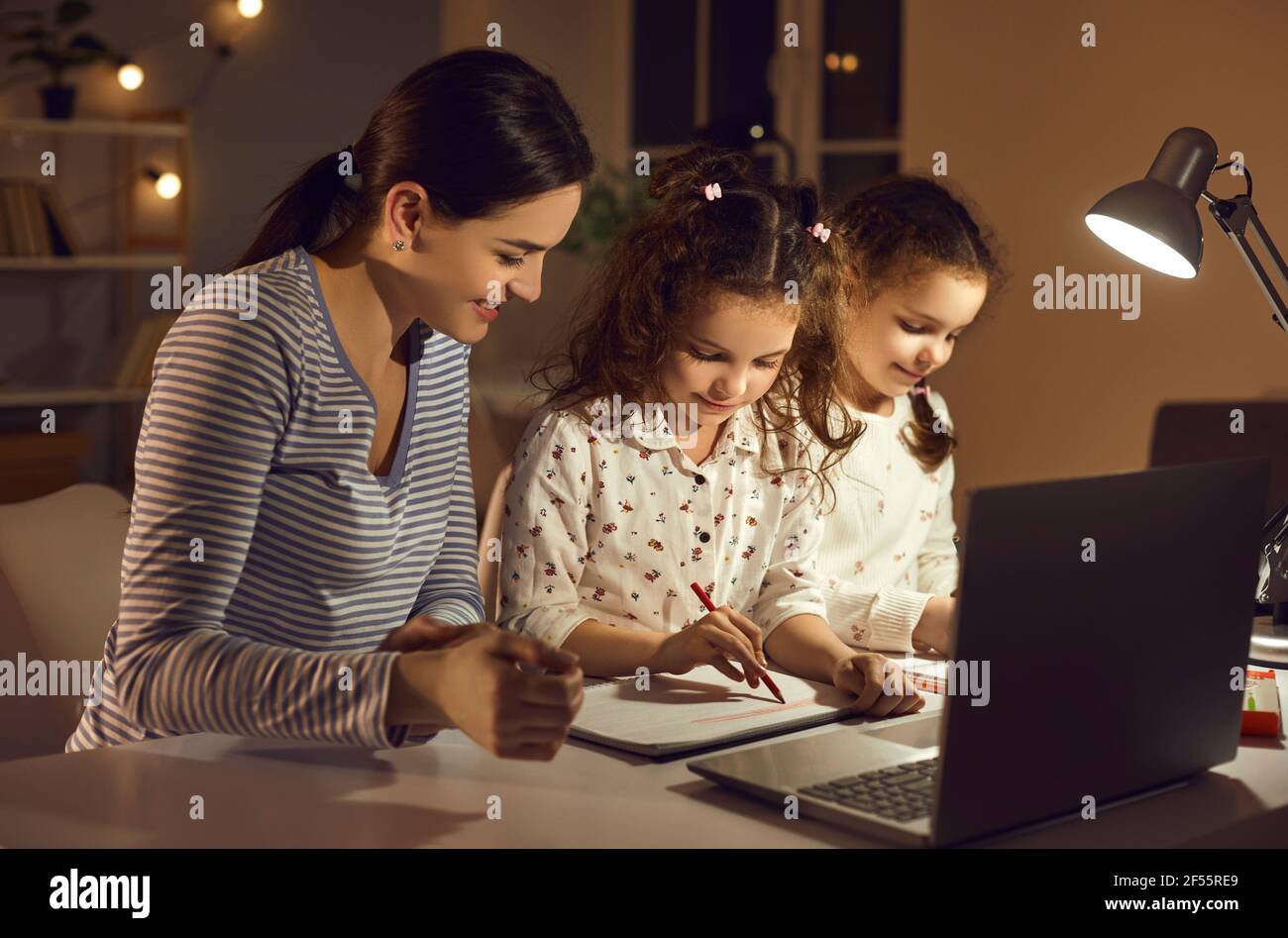 Glückliche Mutter und Kinder sitzen am Schreibtisch zu Hause beschäftigt Mit Hausaufgaben Stockfoto