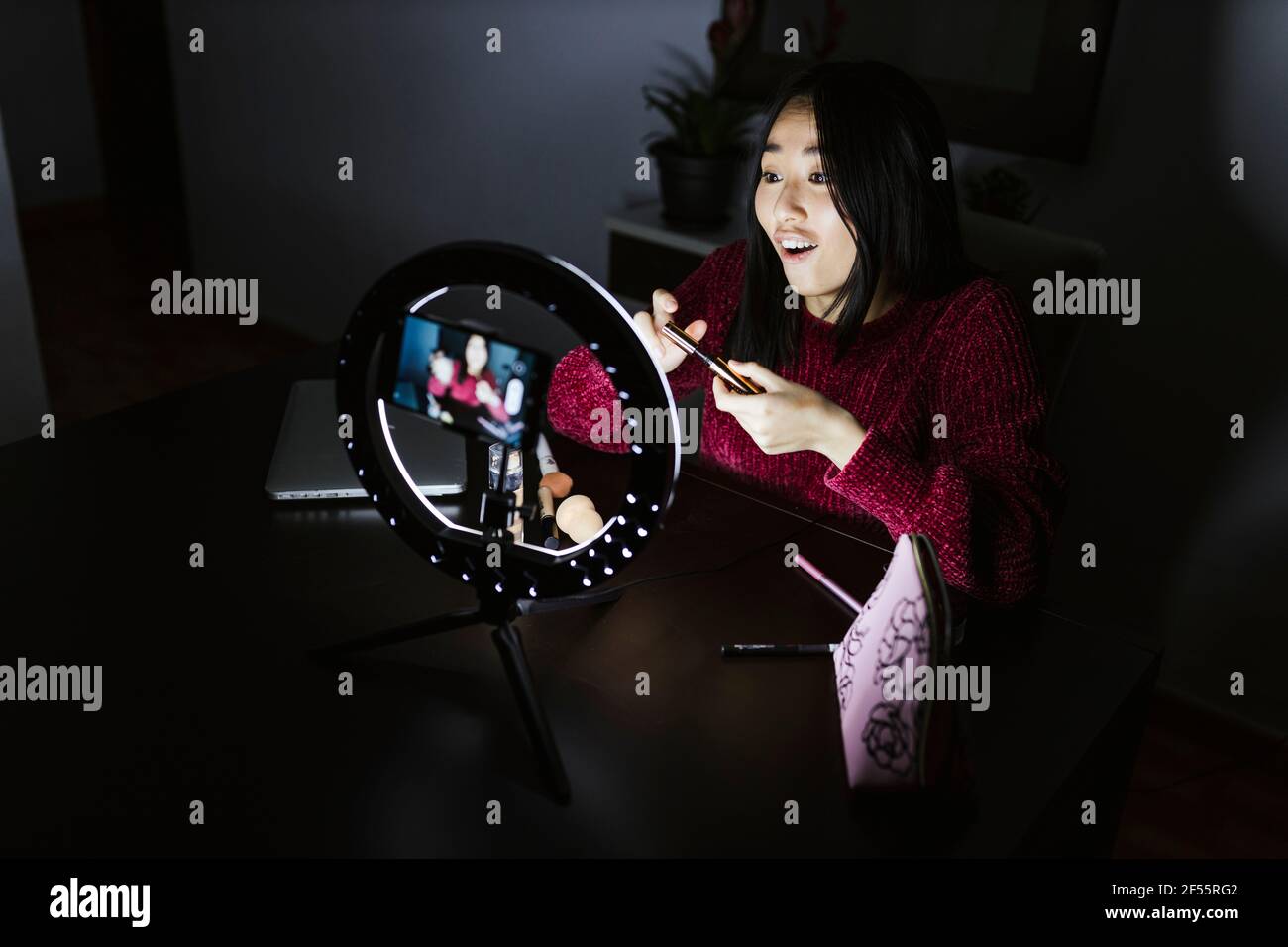 Junge chinesische weibliche Vloggerin erklärt Mascara in der Dunkelkammer Stockfoto