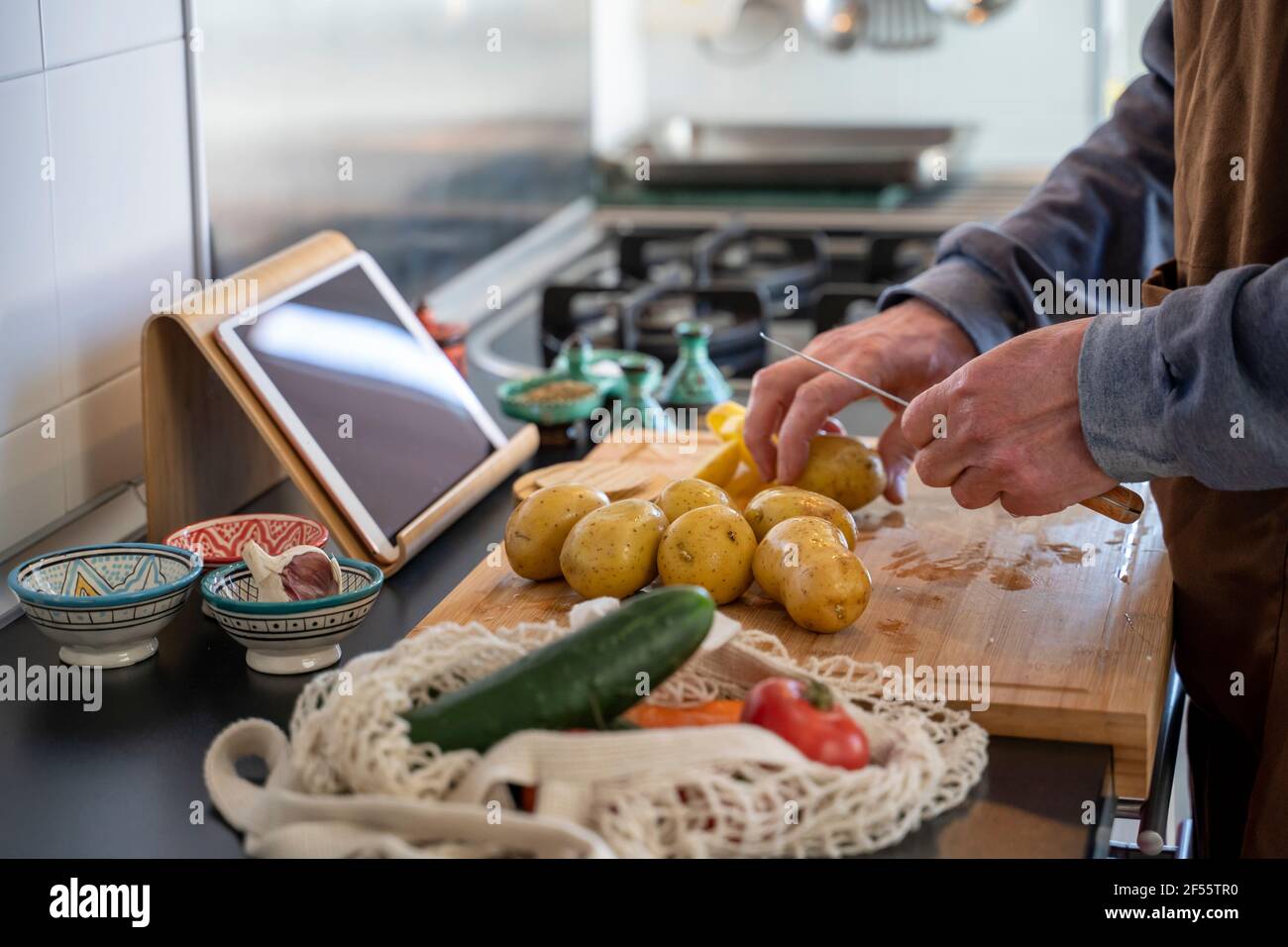 Senior Mann hackt Kartoffeln auf Schneidebrett in der Küche Stockfoto