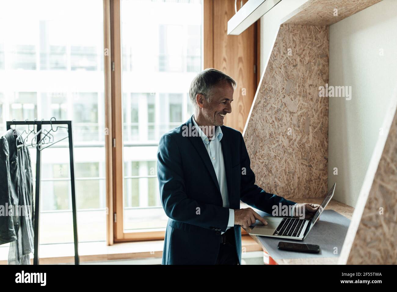 Lächelnder Geschäftsmann mit Laptop, während er in der Lobby im Büro stand Stockfoto