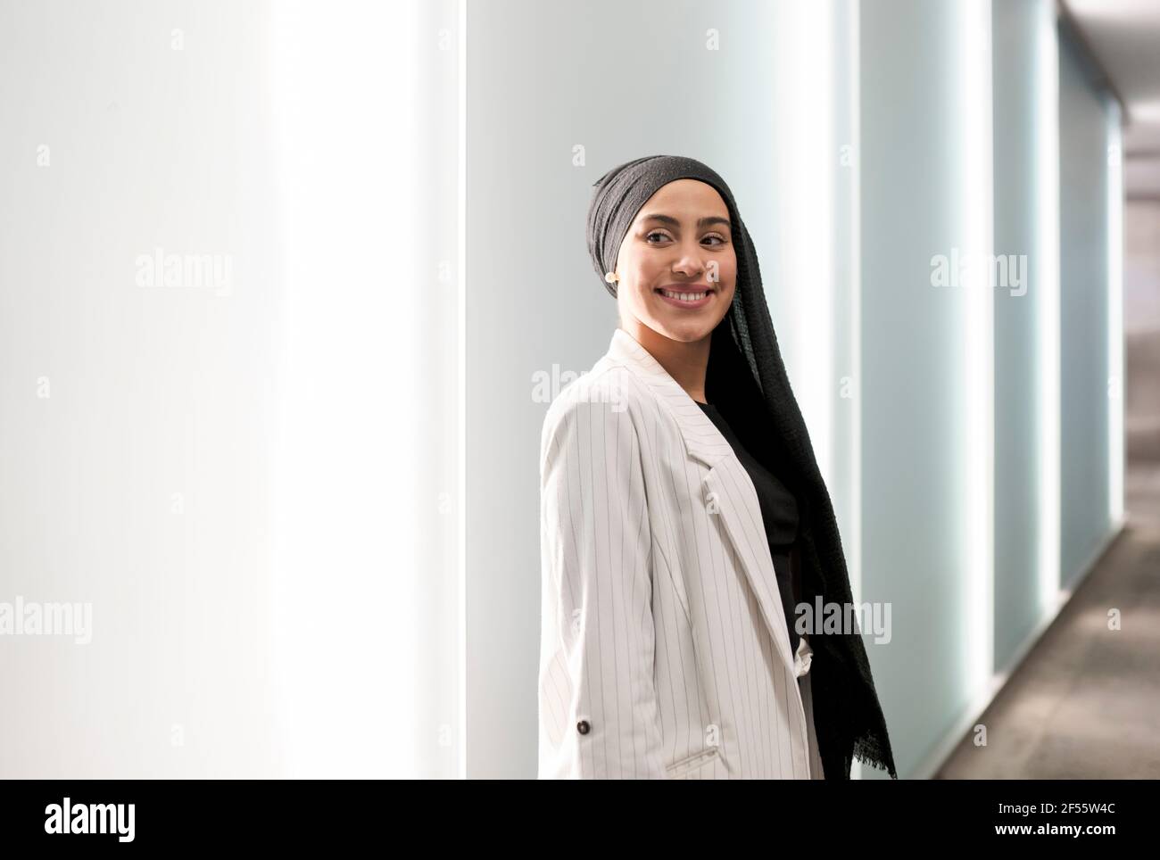 Lächelnde arabische Frau schaut weg, während sie in der Nähe der Mauer steht Einkaufszentrum Stockfoto