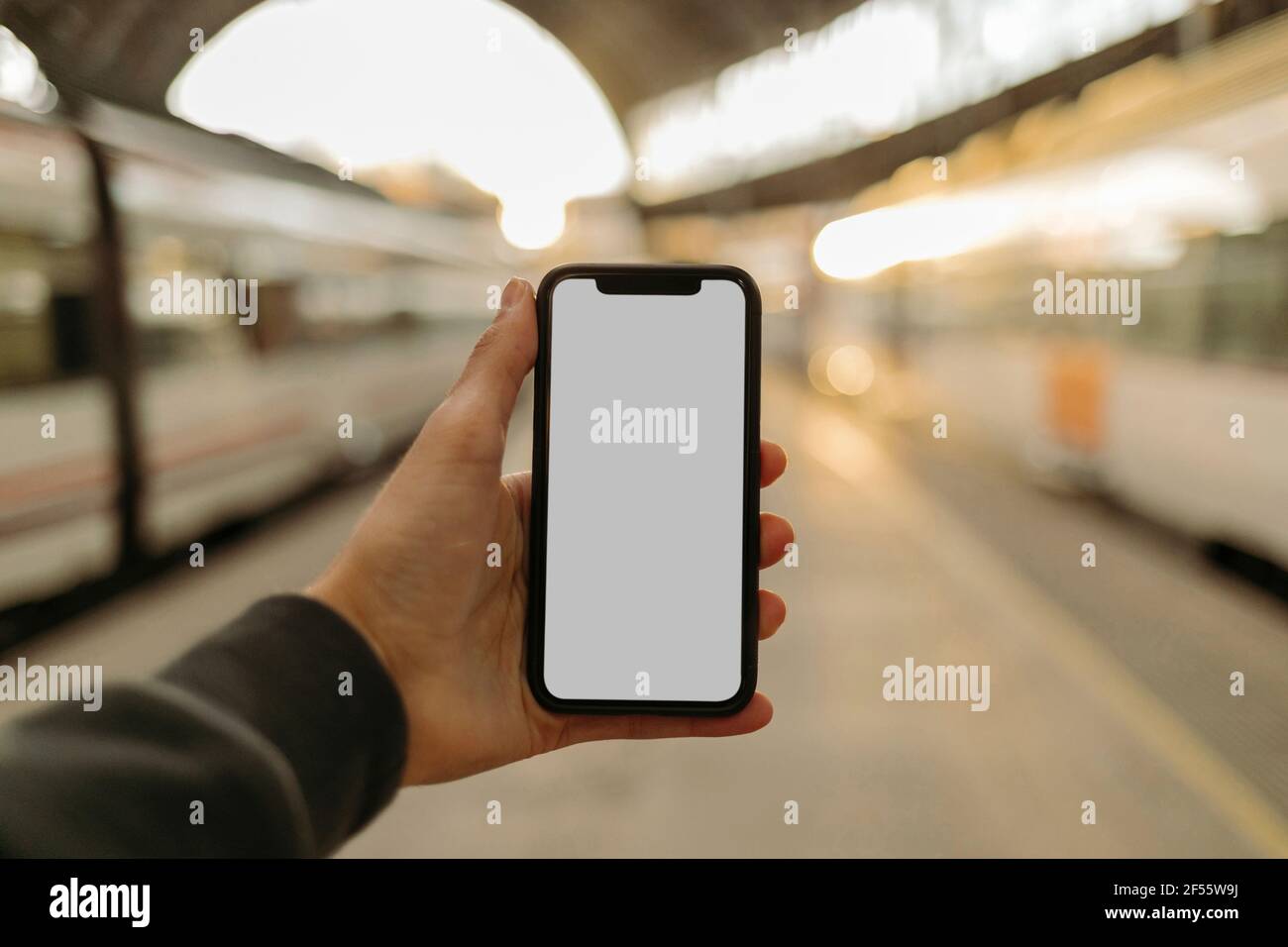 Junger Mann, der am Bahnhof ein Telefon mit leerem Bildschirm benutzt Stockfoto