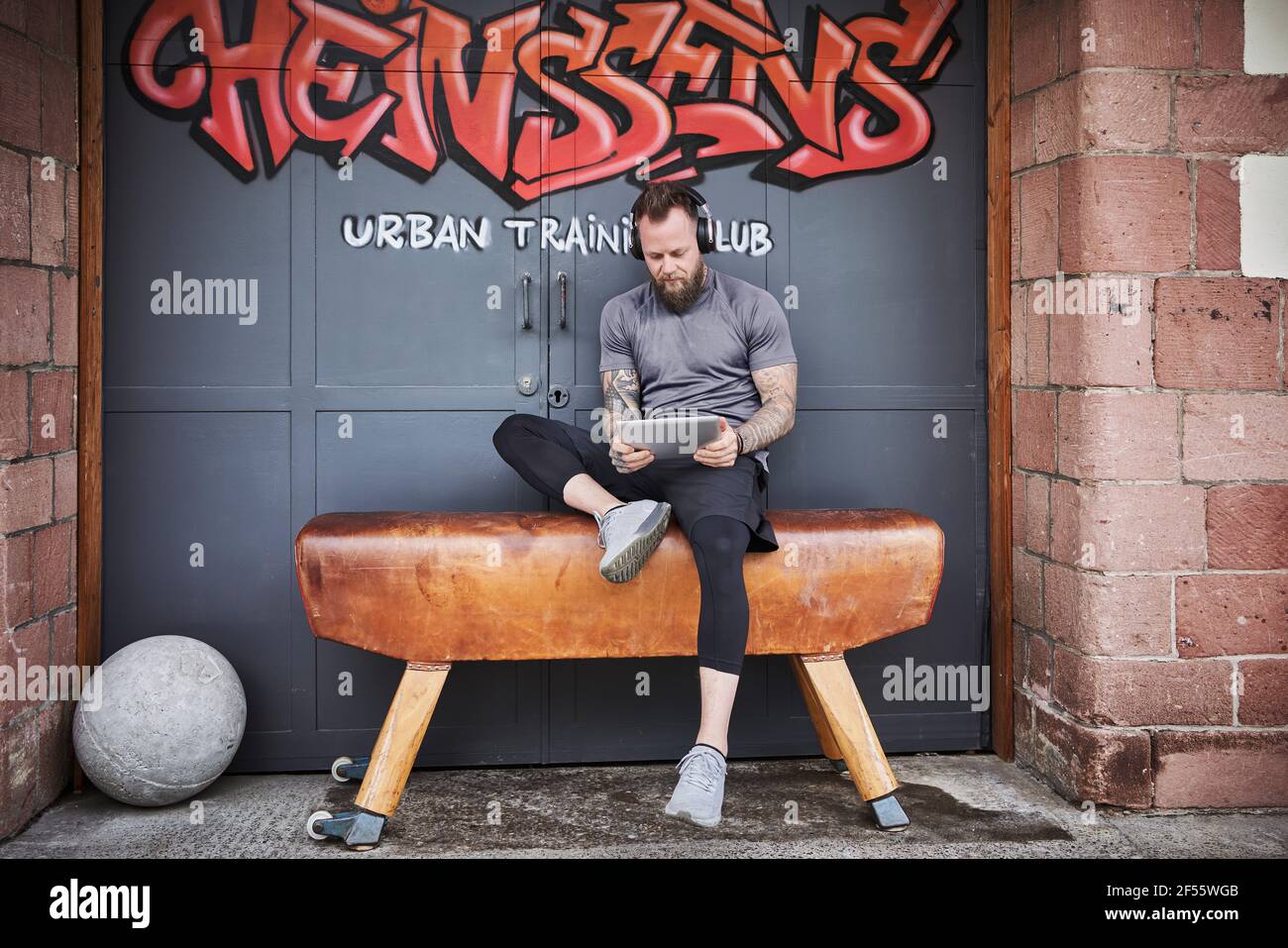 Sportler mit digitalem Tablet, während sie auf der Bank gegen Graffiti sitzen Tür Stockfoto