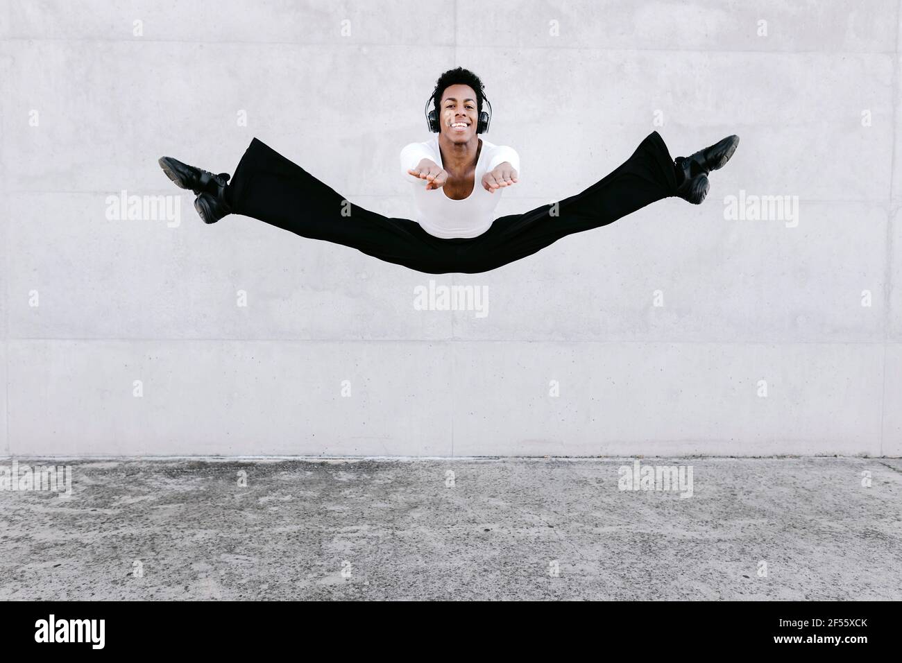Männliche Tänzerin übt Splits in der Luft gegen die Wand Stockfoto