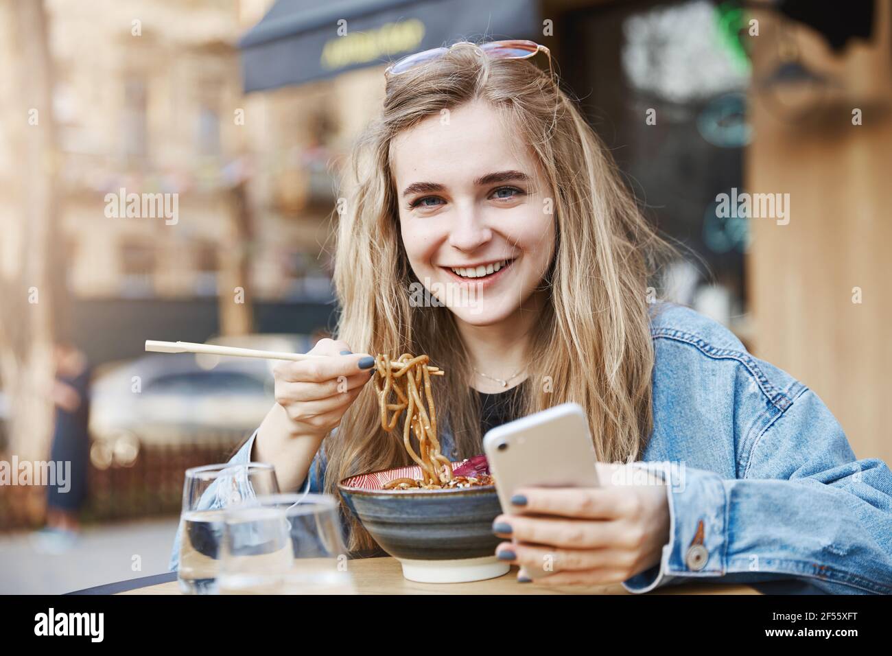 Stilvolle Teenager-Mädchen kann Smartphone nicht verlassen, auch während des Essens. Porträt von zufrieden und glücklich gut aussehende Frau in trendigen Outfit und Brille, halten Stockfoto