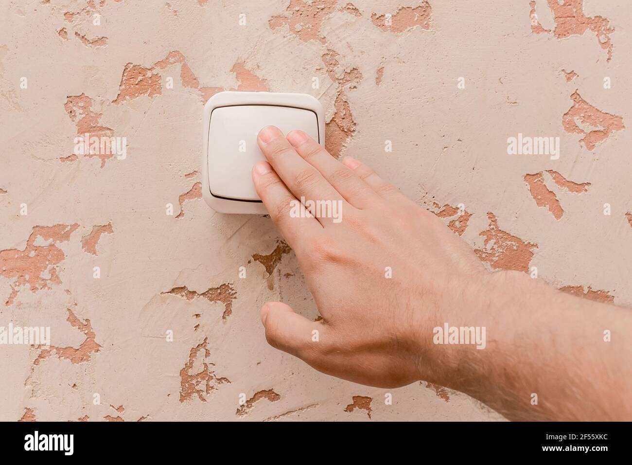 Die Hand des Mannes schaltet das Licht mit einem elektrischen Schalter in einem modernen Raum Innenhintergrund aus. Stockfoto