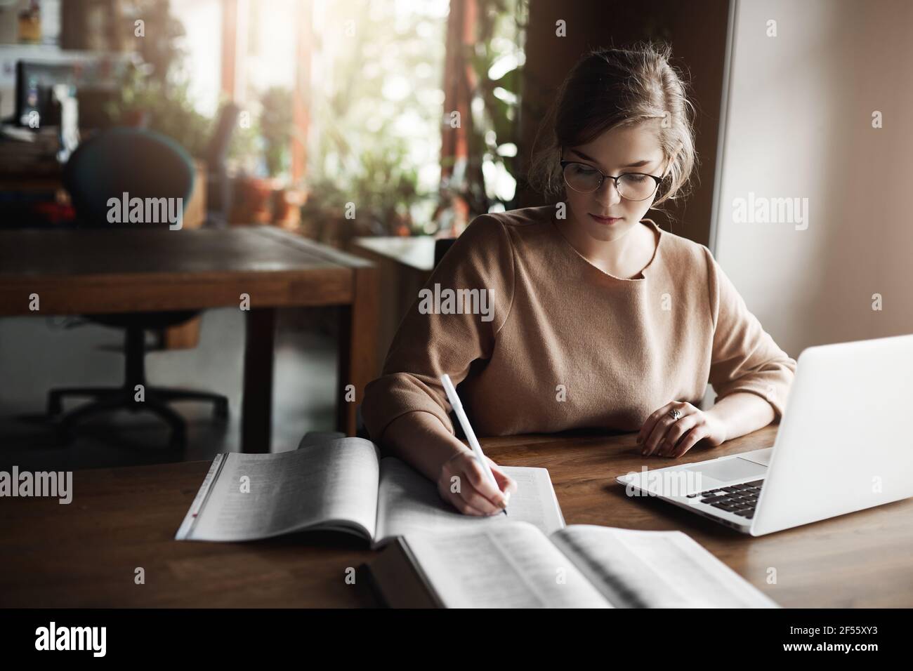 Du kannst Mädchen nicht mit irgendetwas ablenken. Portrait von charmanten fokussierten kaukasischen Schülerin in Brille, Schreiben mit Stift in Notebook, arbeiten mit Stockfoto