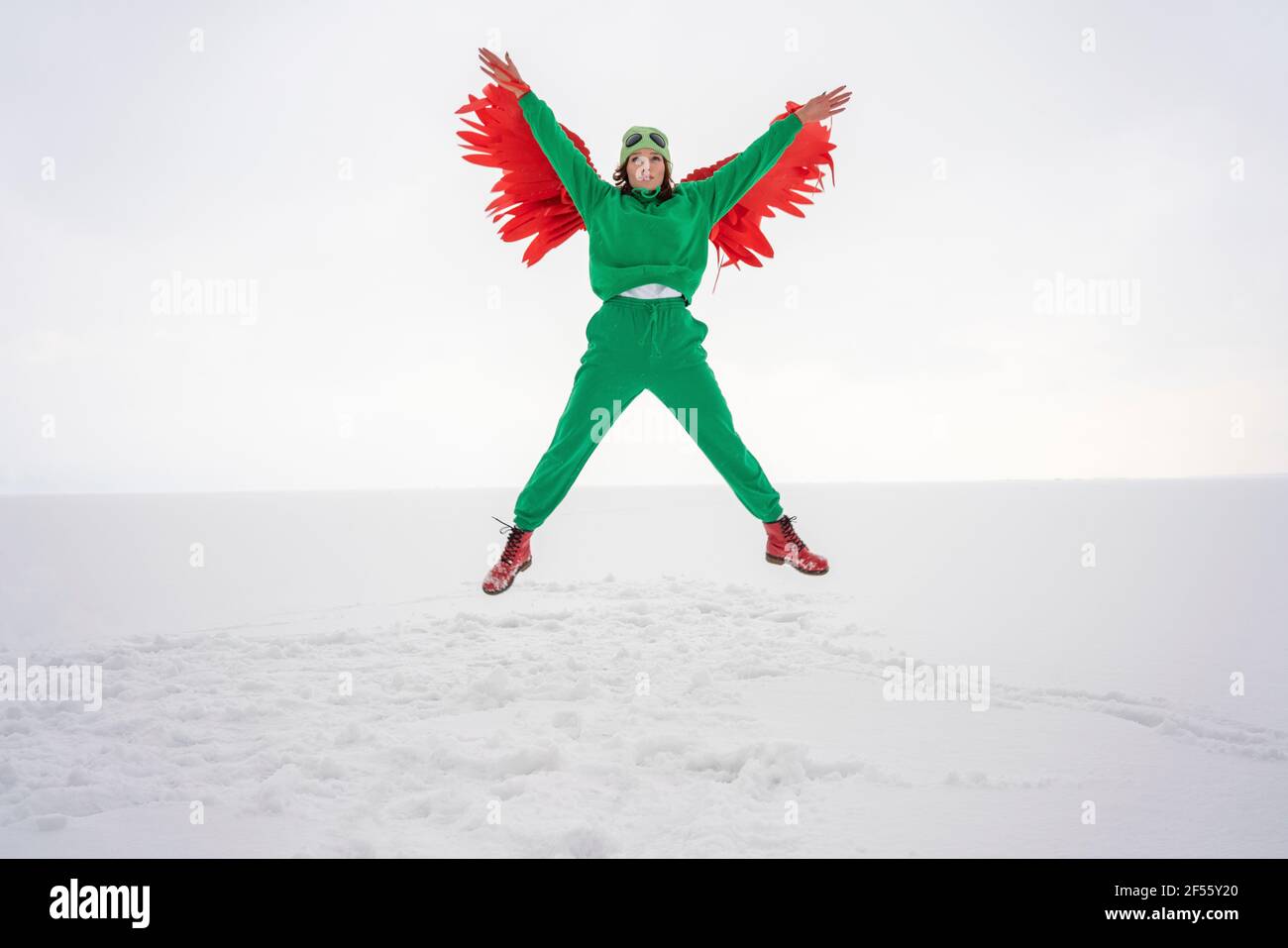 Sorglose Frau im grünen Vogel-Kostüm, die mitten in der Luft gegen sie fliegt Himmel Stockfoto
