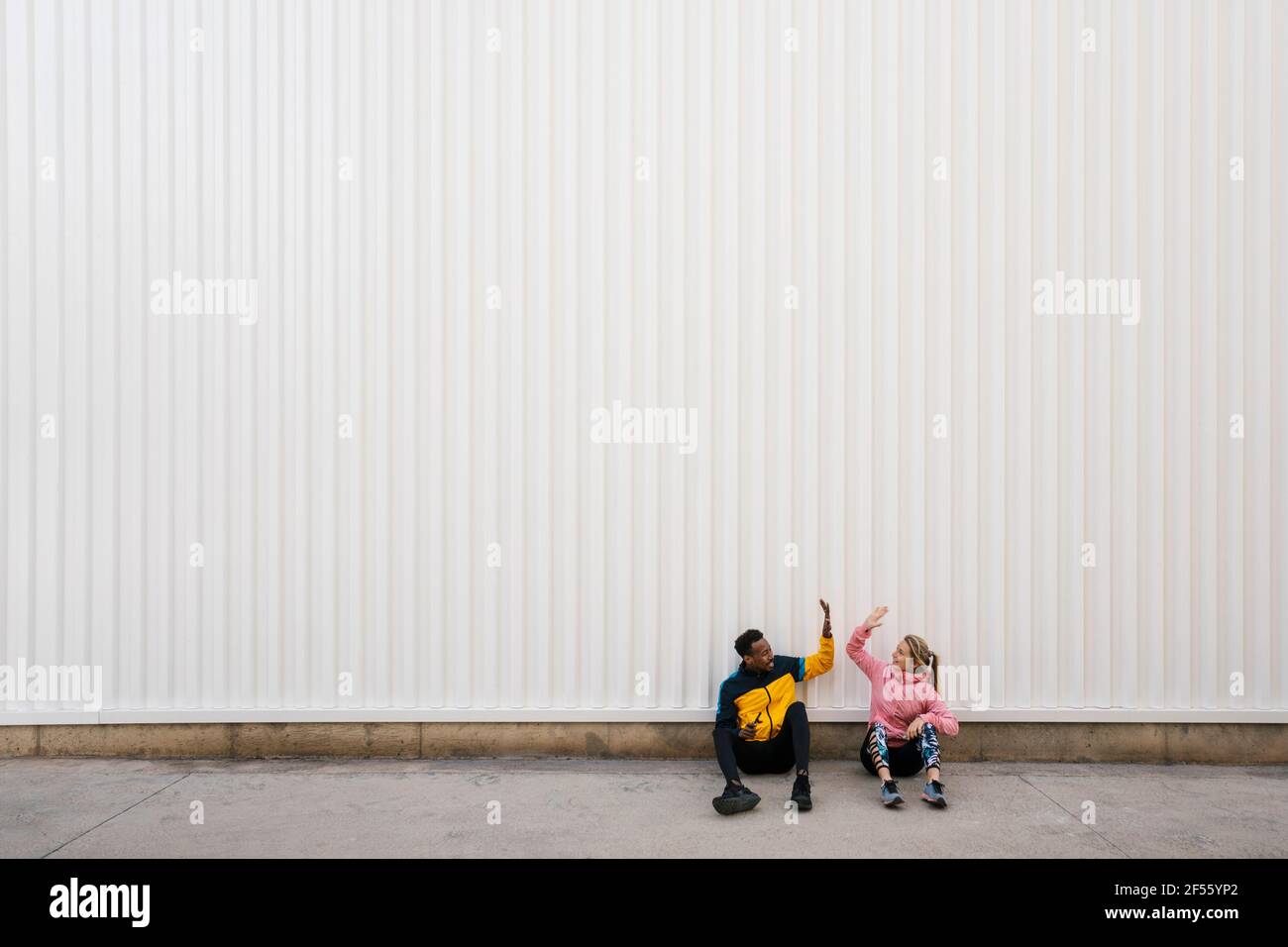 Mann und Frau machen High-Five, während sie auf dem Boden sitzen Wand Stockfoto