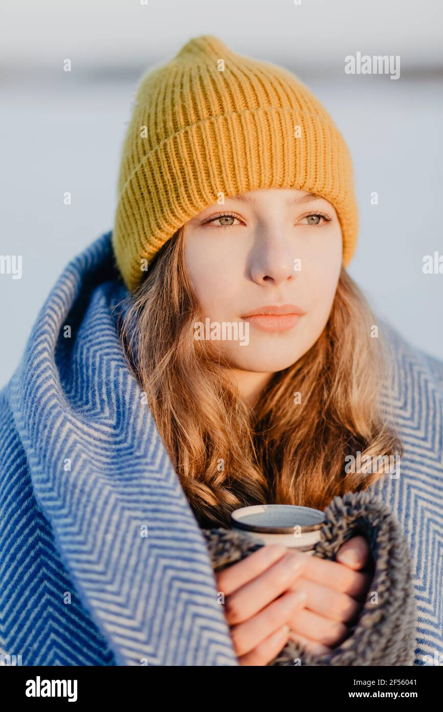 Portrait von schönen Teenager-Mädchen tragen Strickmütze Erwärmung sich Oben mit Wolldecke und Tasse heißen Tee Stockfoto