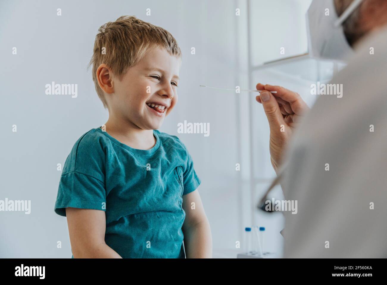 Junge lächelnd, während der Nasenabstrich vom Arzt gesessen wurde Klinik Stockfoto