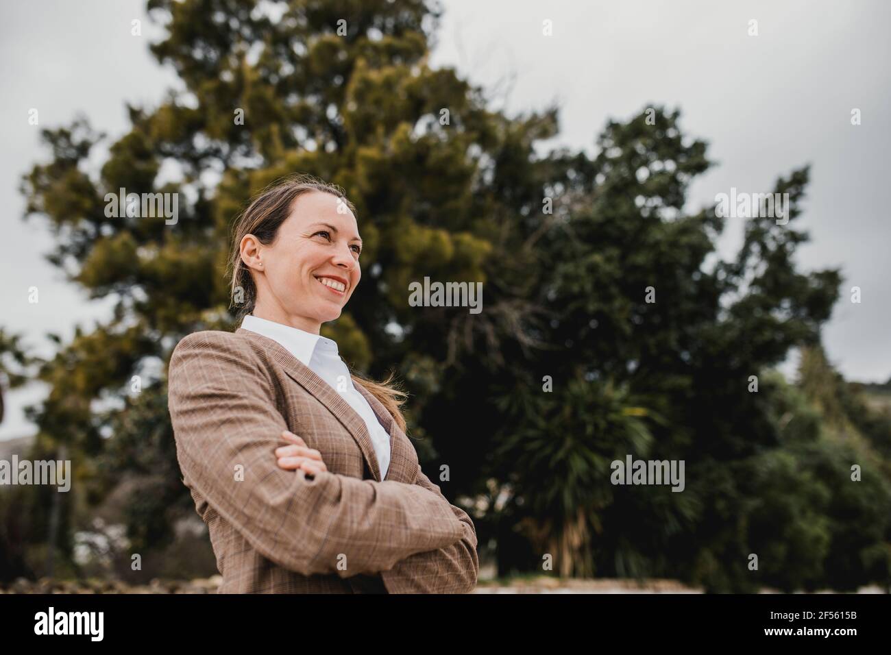 Lächelnde Geschäftsfrau mit gekreuzten Armen, die wegschauen Stockfoto