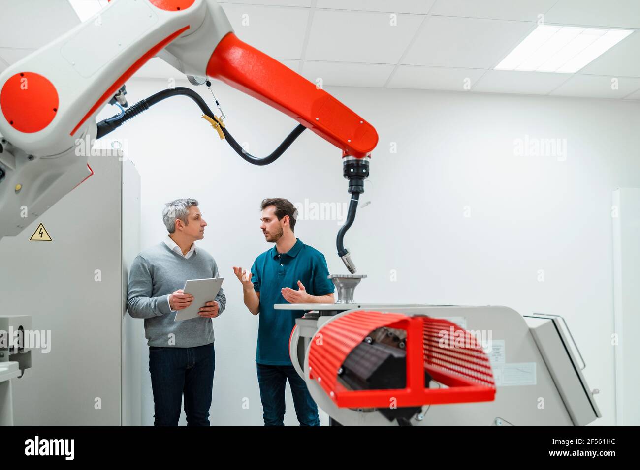 Männliche Ingenieure in legerer Kleidung diskutieren über automatischen Schweißbrenner Im Werk Stockfoto