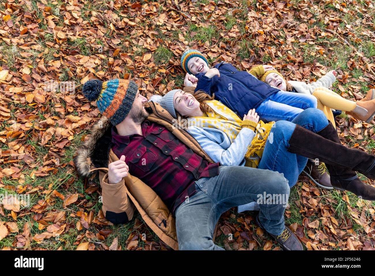 Glückliche Familie beim Spielen, während sie im Wald auf Blättern liegt Stockfoto