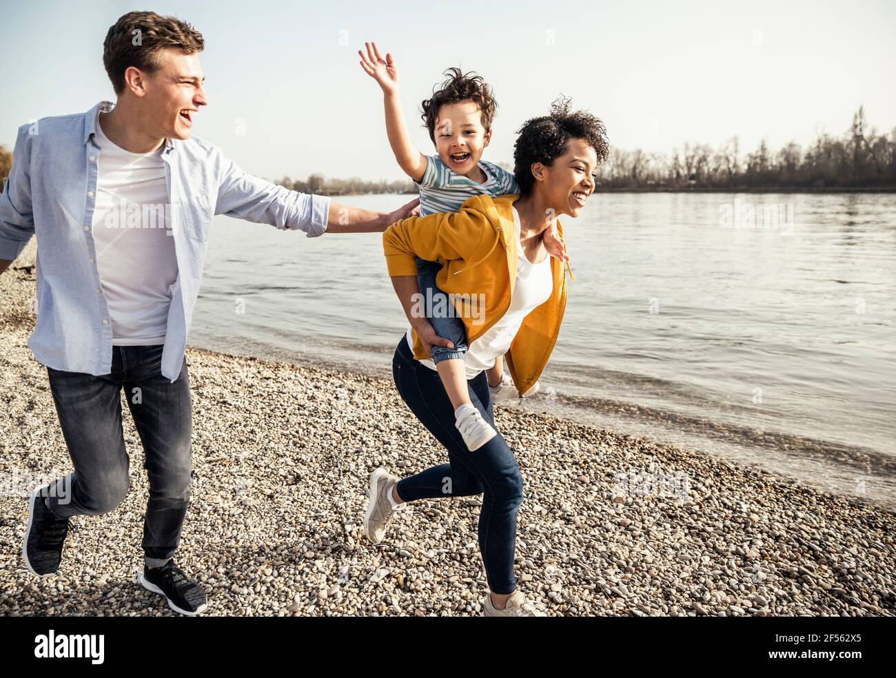 Fröhliche Familie, die Spaß hat, während sie am sonnigen Seeufer läuft Tag Stockfoto