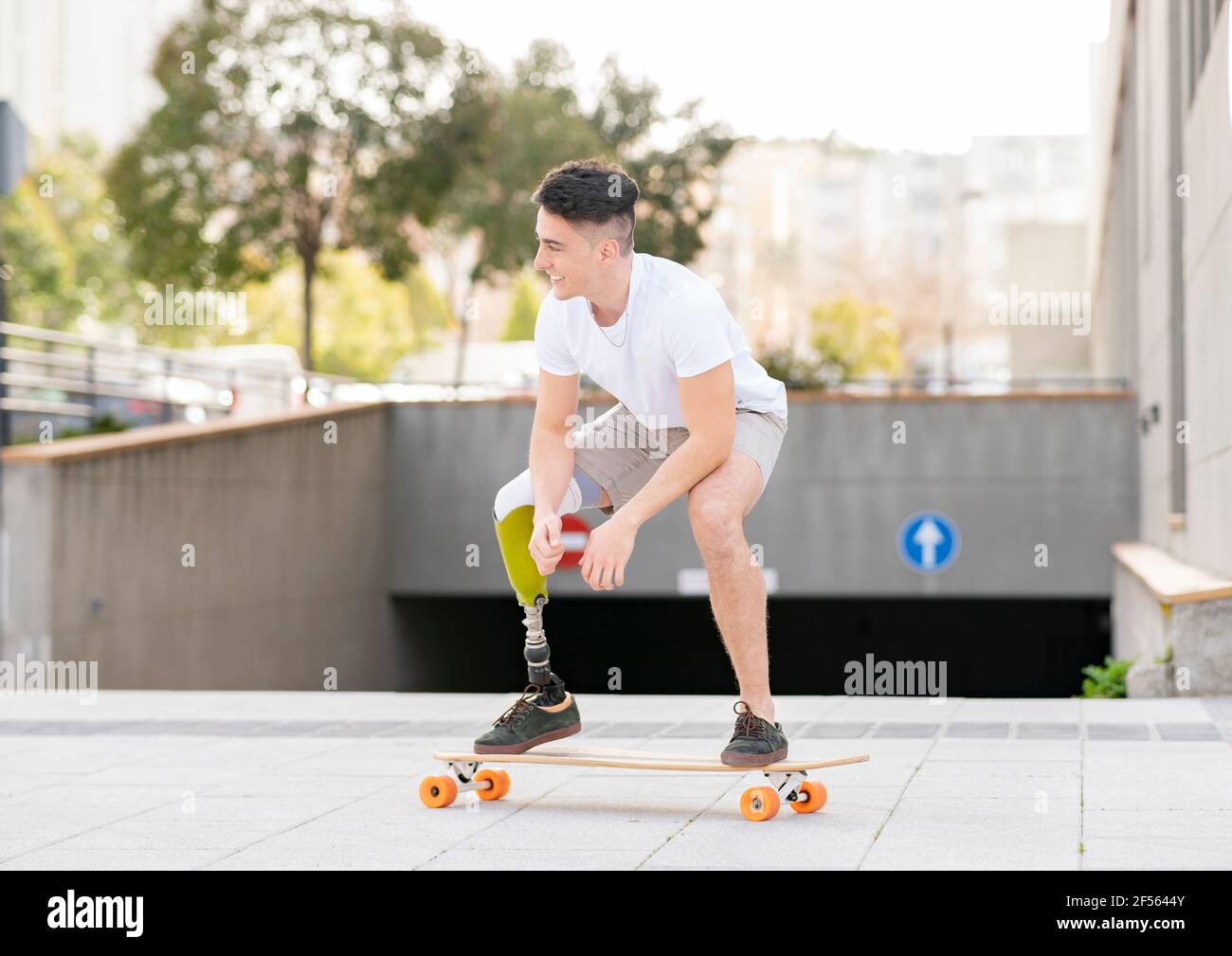 Lächelnd amputierte Mann Skateboarding gegen U-Bahn in der Stadt Stockfoto