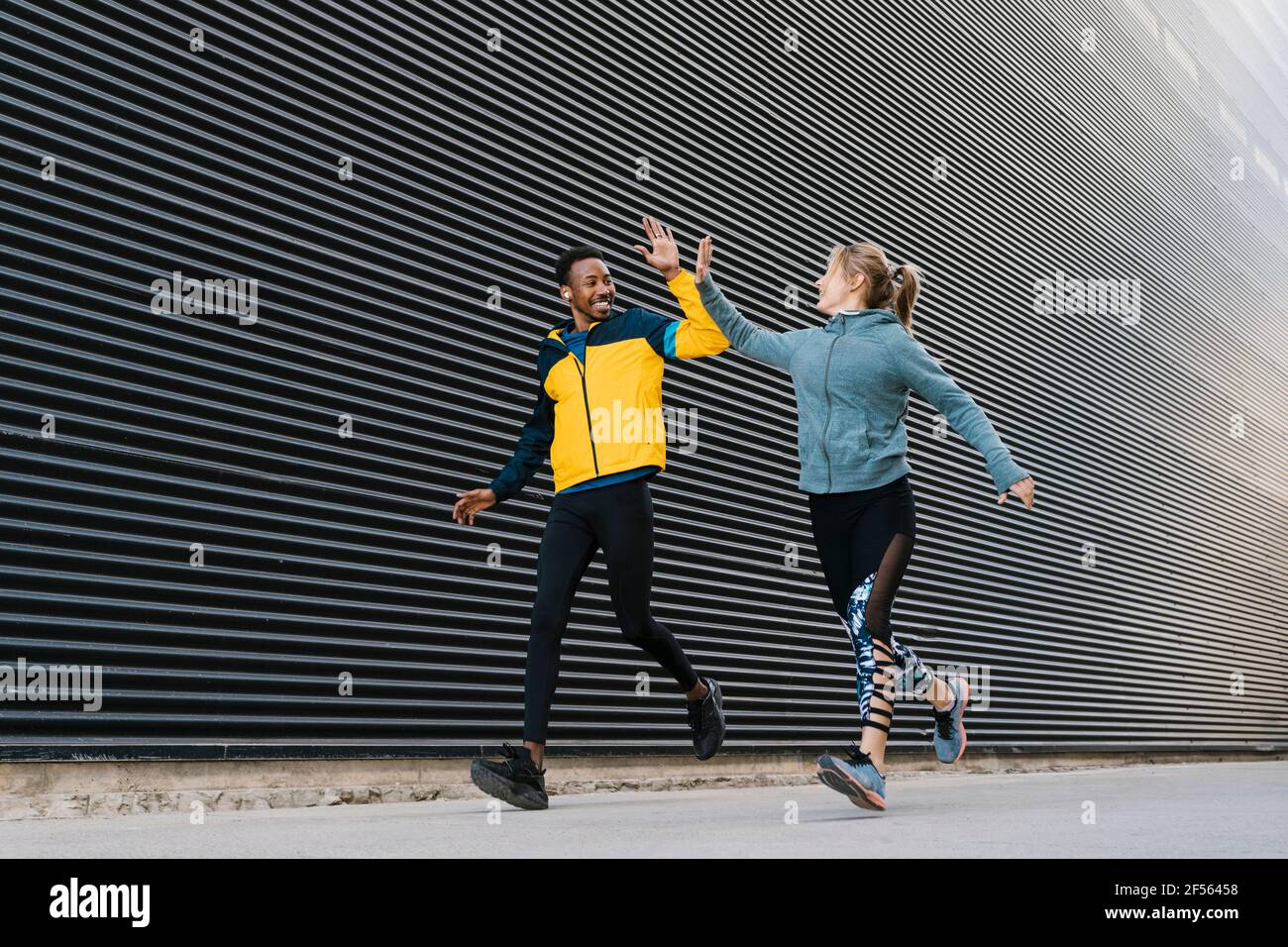 Männliche und weibliche Sportsperson, die beim Laufen auf dem Bürgersteig High-Five-Punkte macht Beim Sporttraining an der Wand Stockfoto