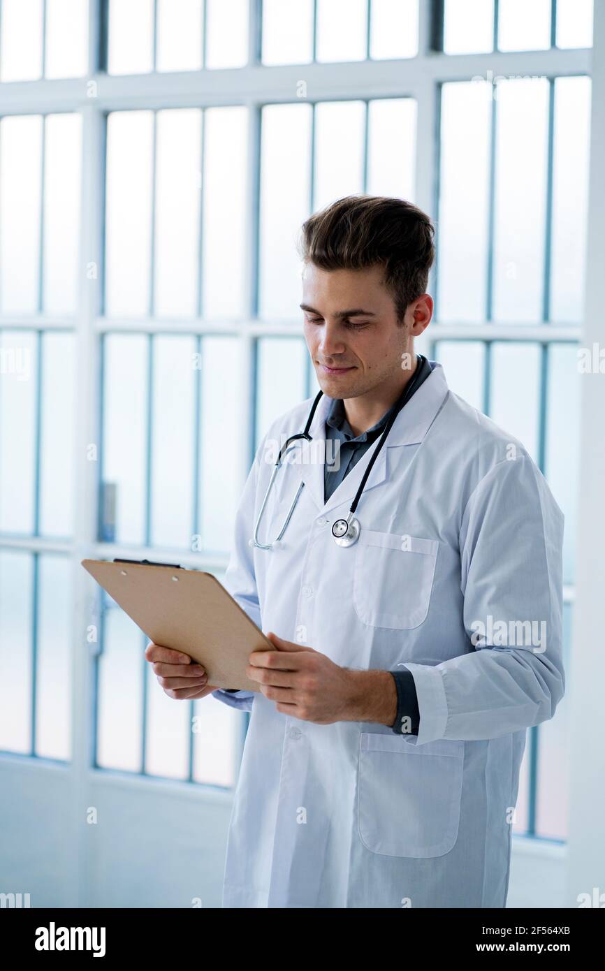 Männlicher Arzt, der Dokumente ansieht, während er die Zwischenablage im Krankenhaus hält Stockfoto