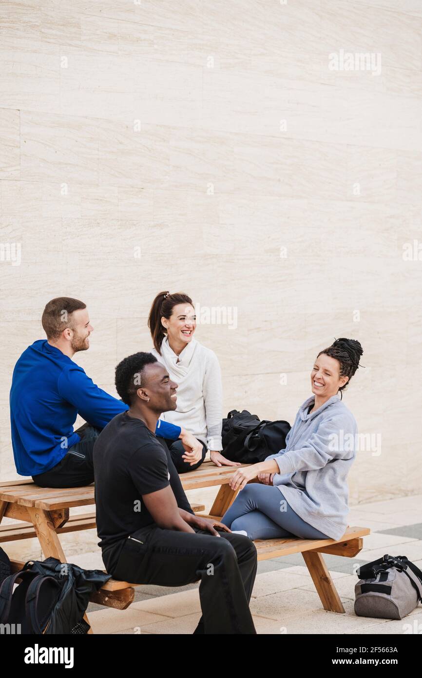 Multiethnische Gruppe von Athleten, die lachen, während sie auf der Bank sitzen Stockfoto