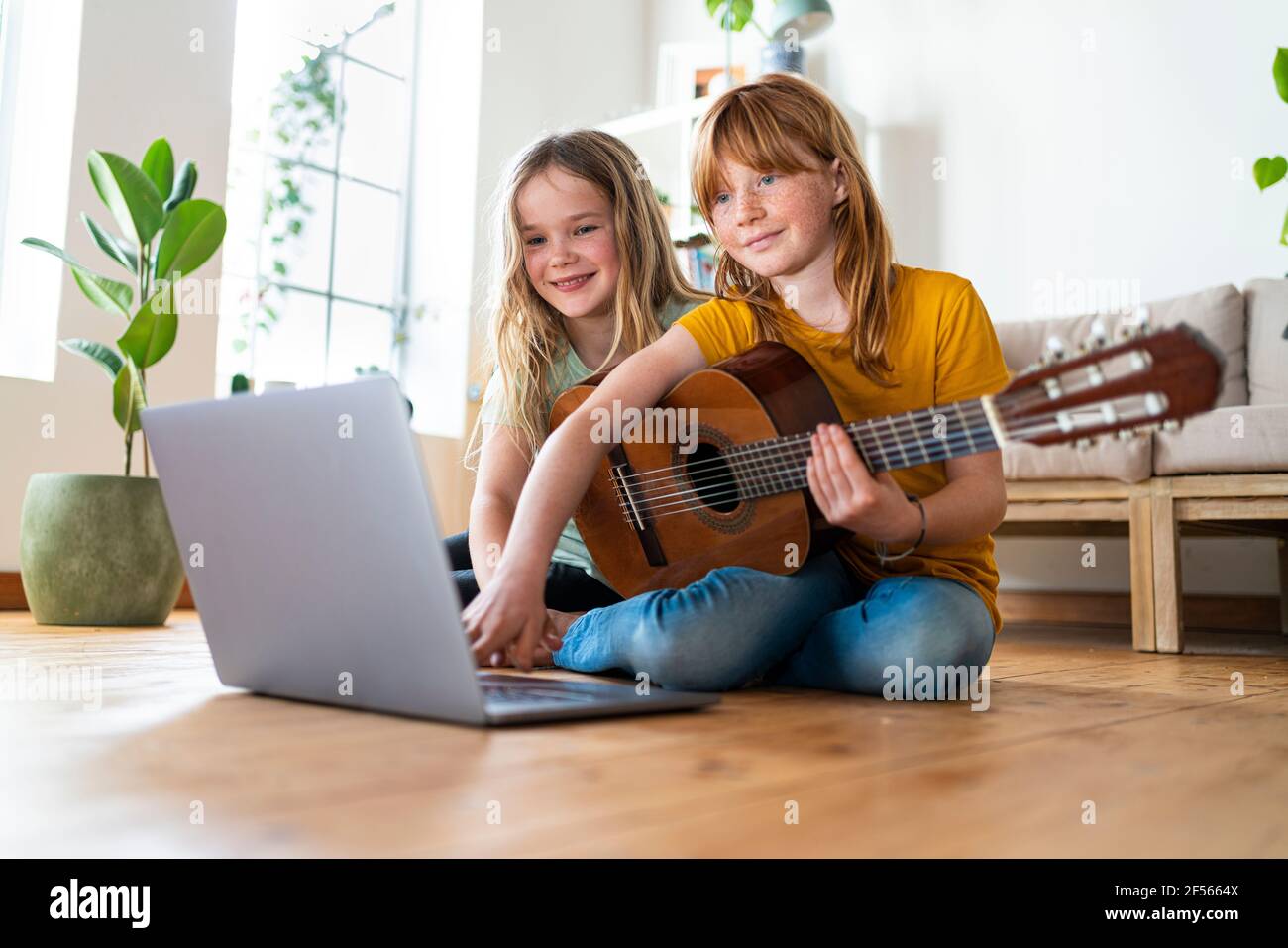 Lächelnde Mädchen E-Learning Gitarre Tutorial durch Laptop im Wohnzimmer Zu Hause Stockfoto