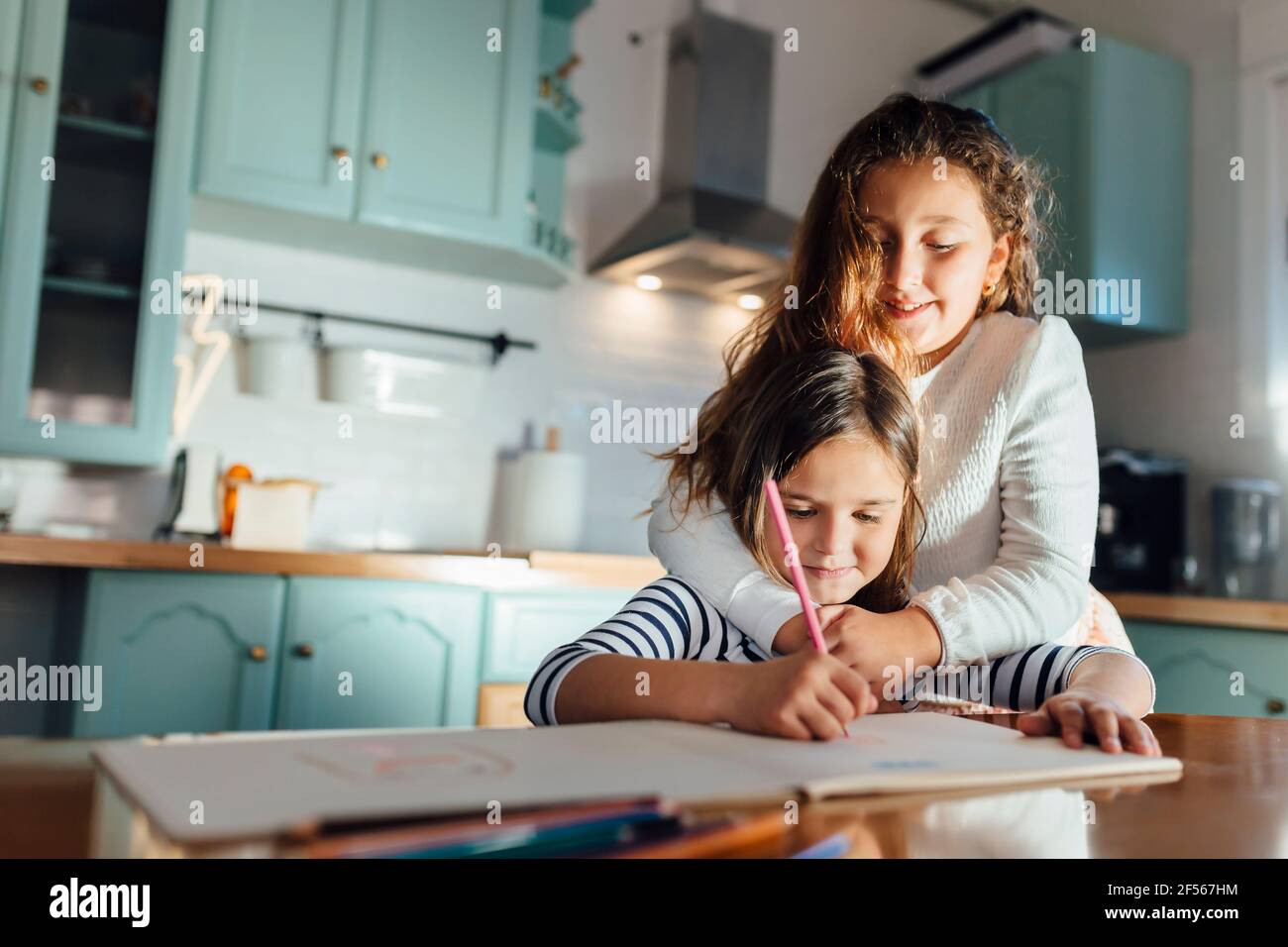 Mädchen Färbung auf Papier, während Schwester umarmt von hinten in Küche Stockfoto