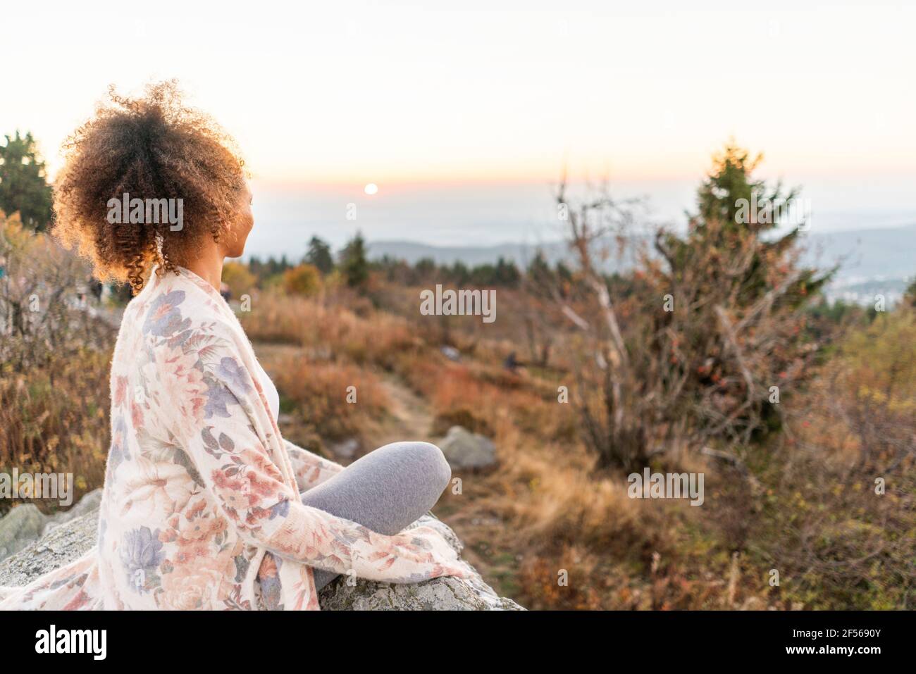 Frau mit lockigen braunen Haaren praktiziert Yoga während des Sonnenuntergangs Stockfoto