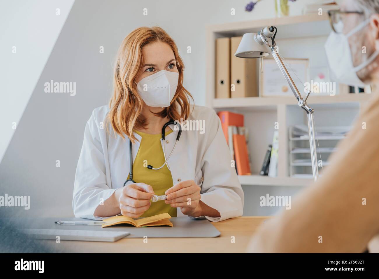 Allgemeinpraktikerin diskutiert über Impfpass mit Patient bei Büro Stockfoto