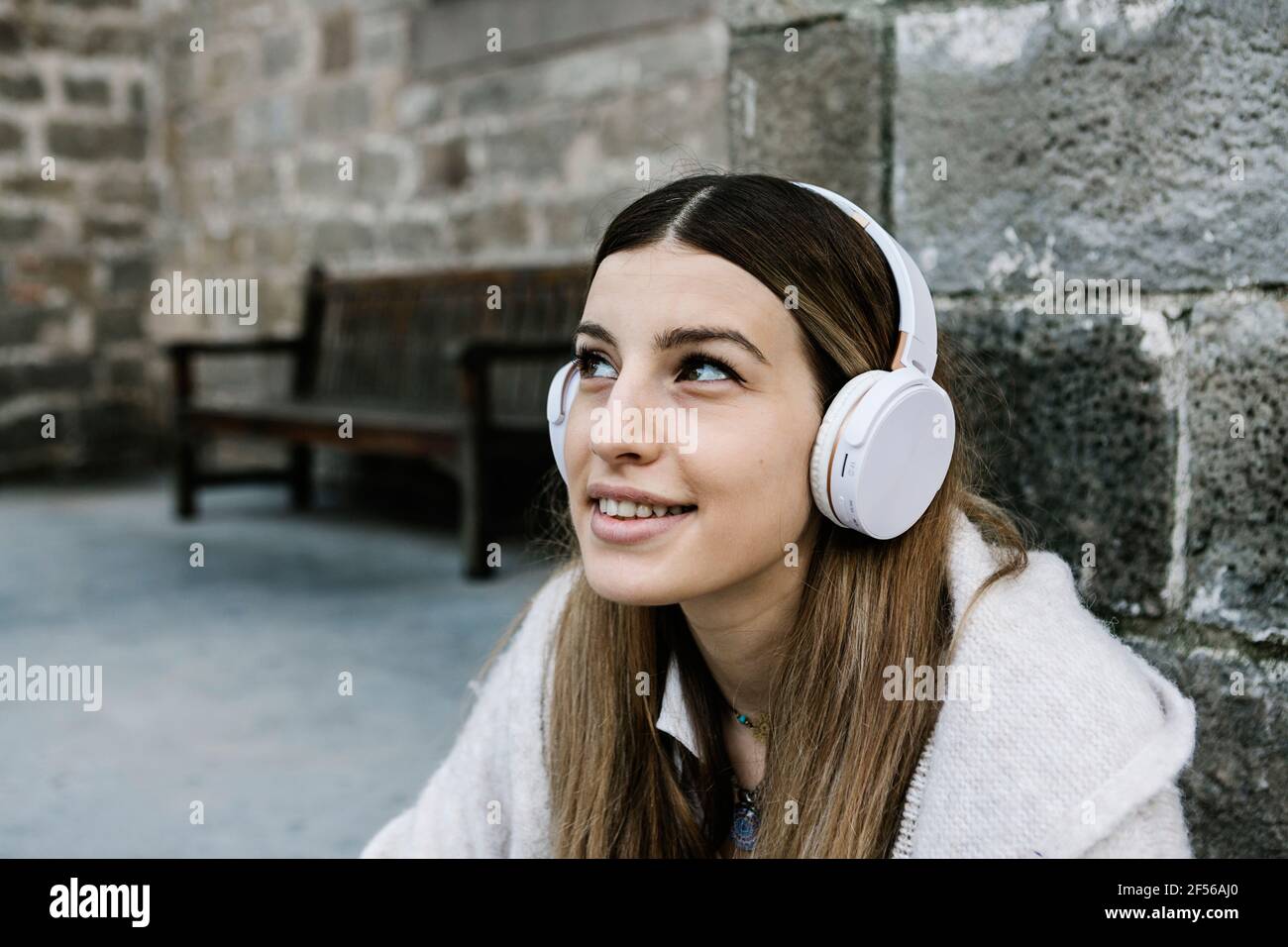 Lächelnde Frau mit Kopfhörern an der Steinwand Stockfoto