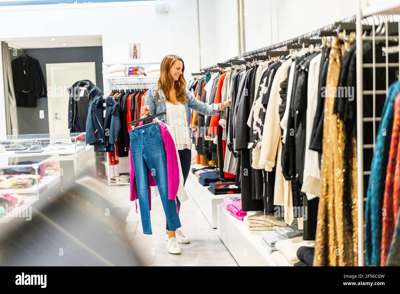 Lächelnde blonde Frau, die beim Einkaufen Kleiderständer in der Hand hält Im Boutique-Stil Stockfoto