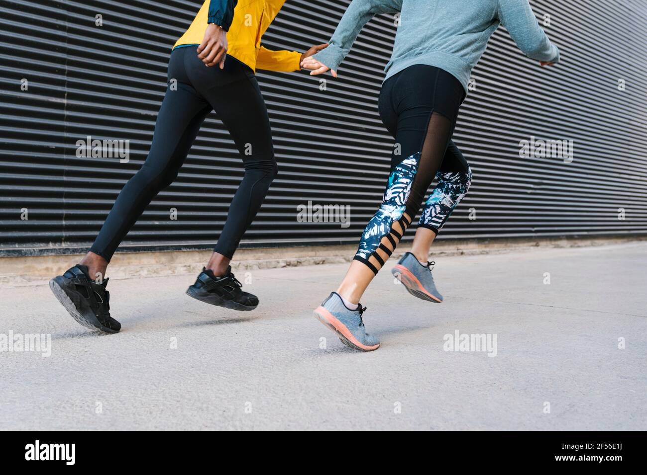 Eine Athletin und ein Athlet, die gemeinsam auf dem Bürgersteig an der Wand laufen Stockfoto