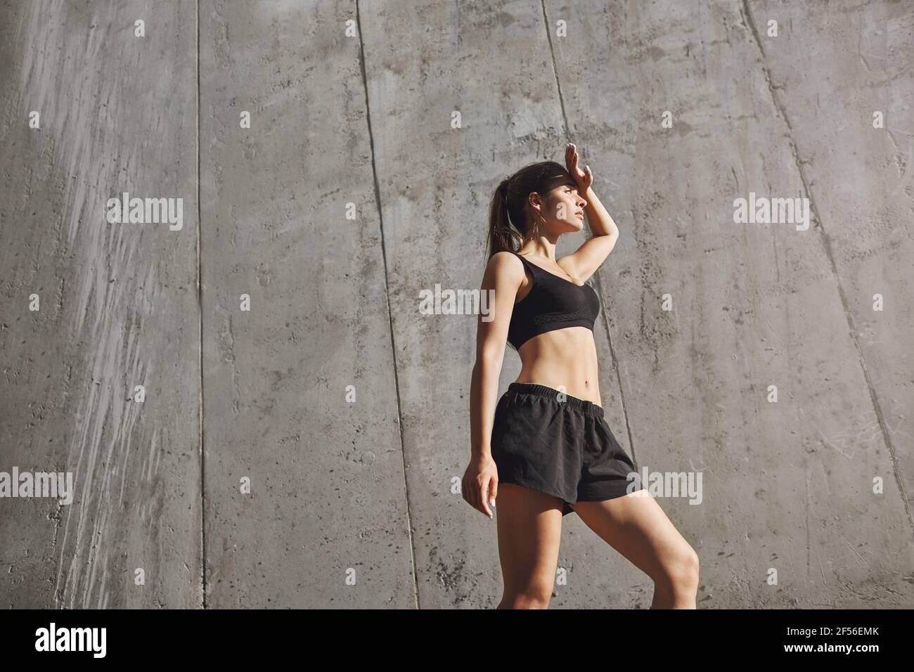 Angenehme Müdigkeit nach dem Training. Low-Angle SHOT Fit Sportlerin in Sport-BH und Shorts, wischen Schweiß von der Stirn, decken die Augen von Sonne aussehen Stockfoto