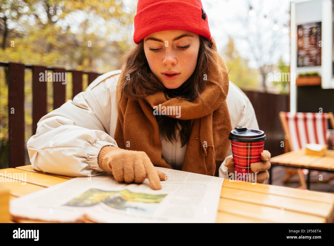Frau mit Kaffeetasse, die Zeitung liest, während sie auf dem Bürgersteig sitzt Café Stockfoto