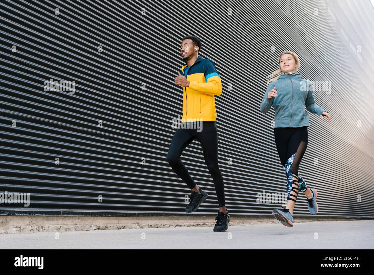 Männliche und weibliche Athletinnen, die während des Sporttrainings auf dem Bürgersteig laufen An der Wand Stockfoto