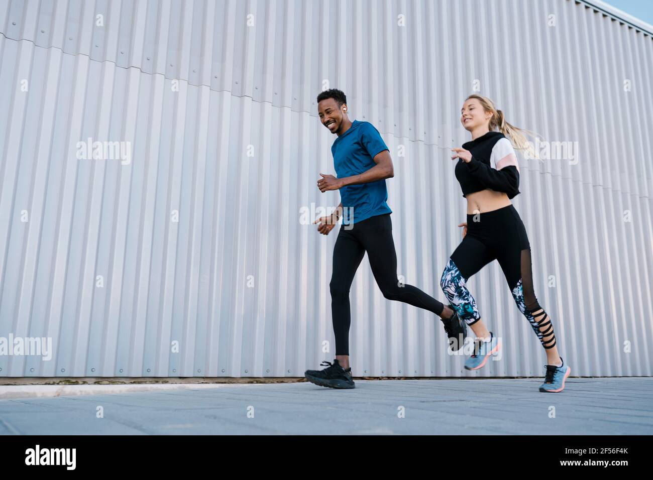 Lächelnder Athlet und Athlet, die auf dem Bürgersteig an der Wand laufen Während des Sporttrainings Stockfoto