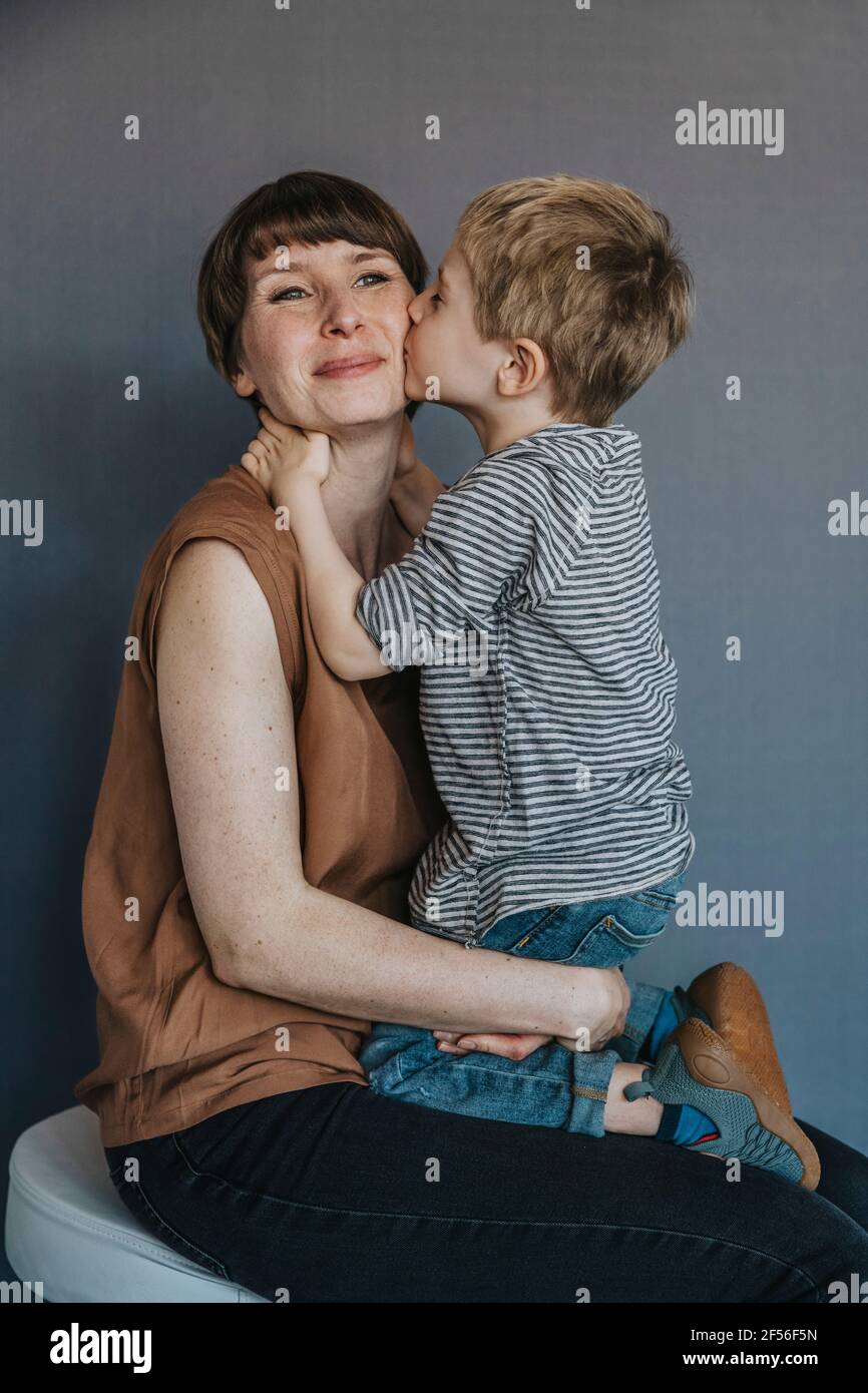 Netter Junge küsst Mutter auf Wange über grauem Hintergrund Stockfoto