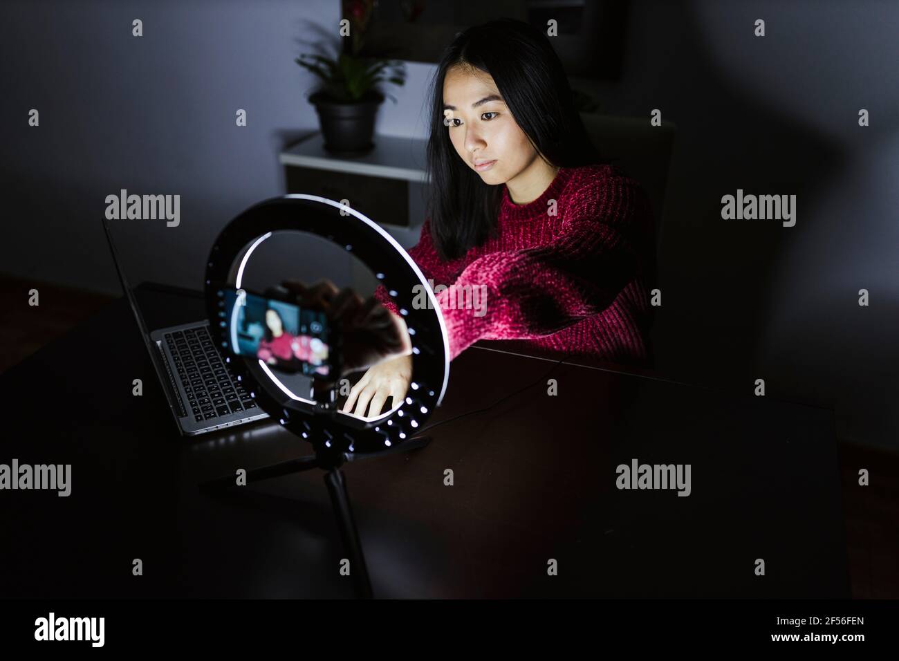 Junge chinesische weibliche Vloggerin, die mit Laptop und beleuchtetem Ring sitzt Leicht Stockfoto