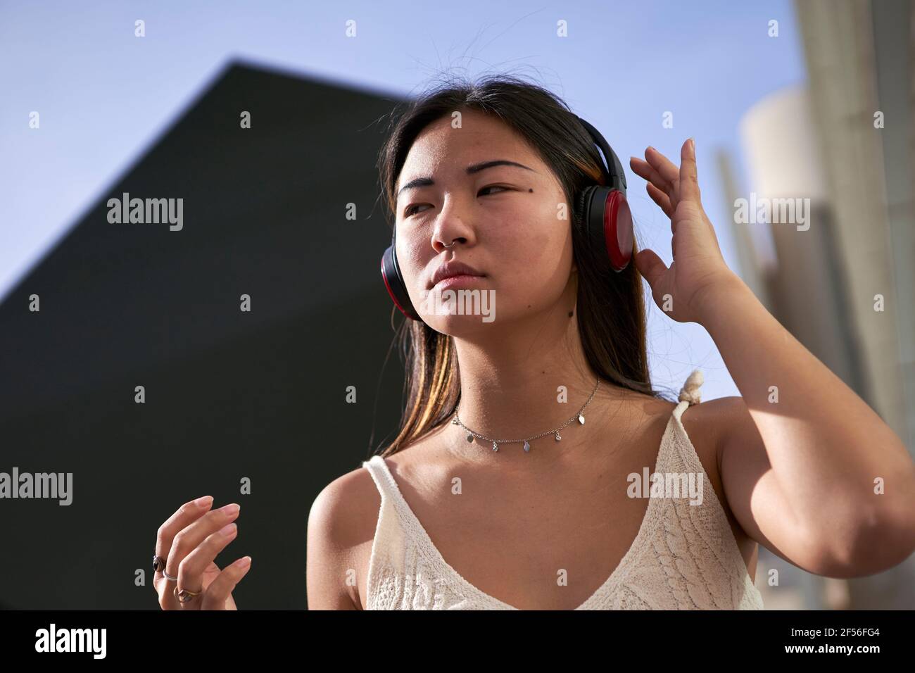 Asiatische Frau schaut weg, während sie Musik über Kopfhörer hört Sonniger Tag Stockfoto