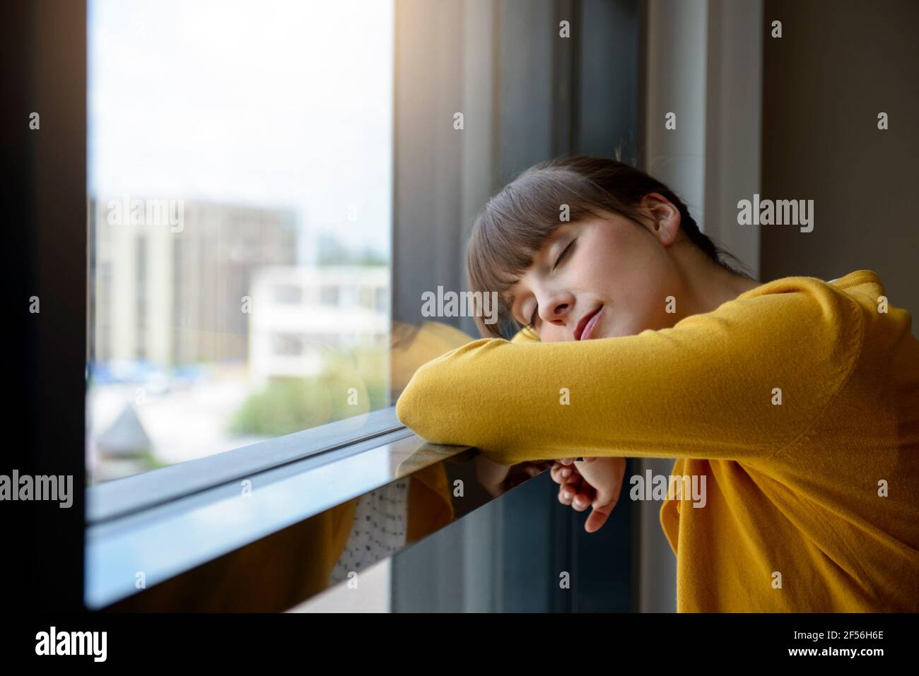 Eine Frau, die ein Nickerchen machte, während sie sich im Büro am Fenster lehnte Stockfoto