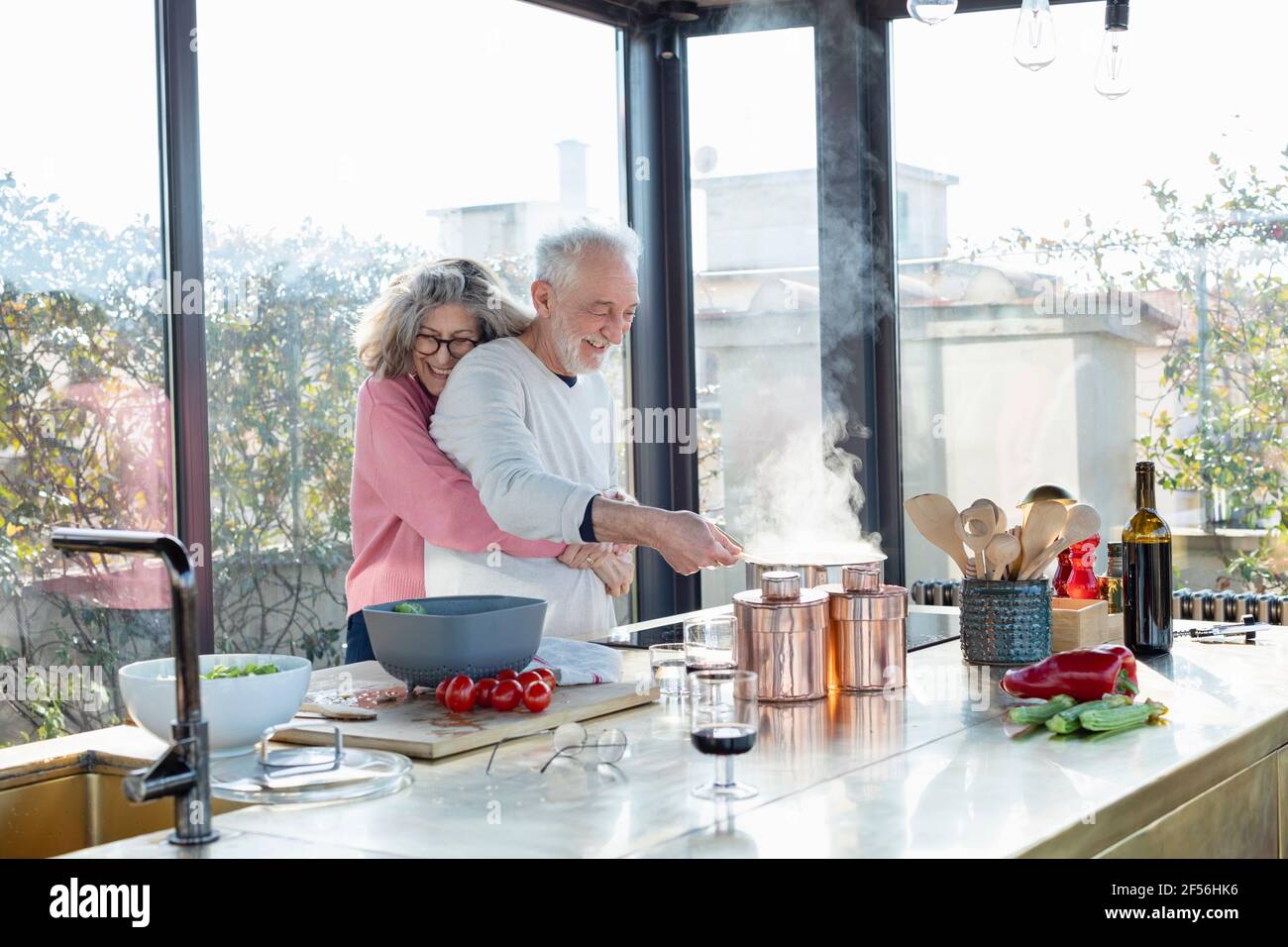 Lächelnde ältere Frau umarmt Mann von hinten in der Küche Zu Hause Stockfoto
