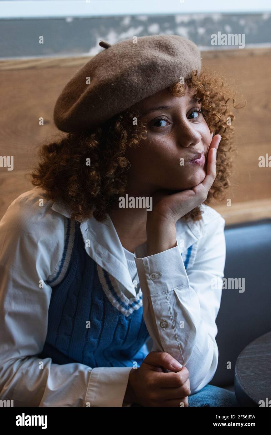 Teenager-Mädchen trägt Baskenmütze macht Gesicht, während mit der Hand sitzen Am Kinn im Café Stockfoto