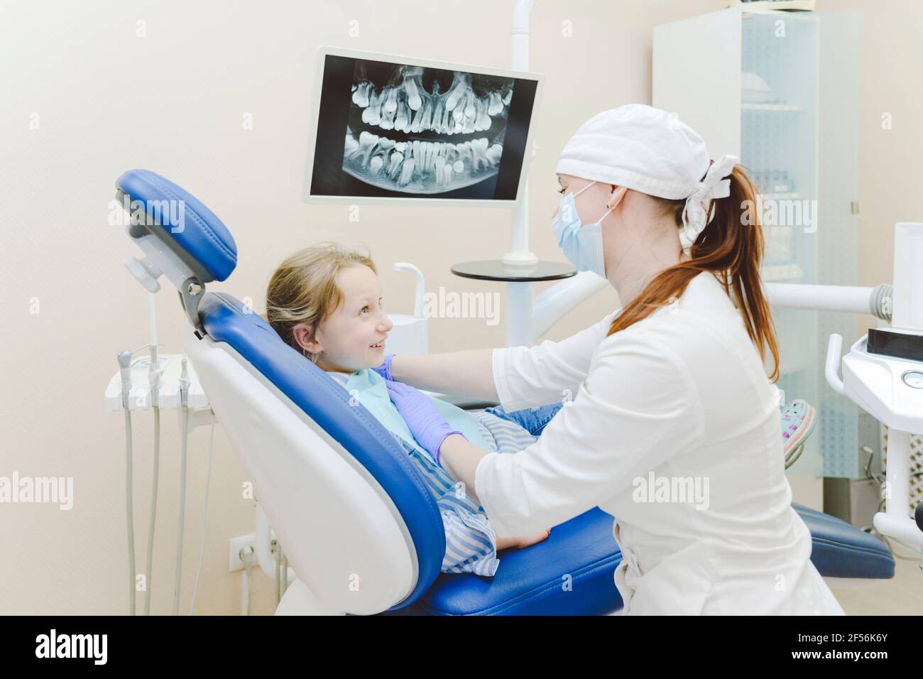 Weibliche Zahnärztin, die Zahndrapieren auf ein kleines Mädchen legt, das darin sitzt Zahnarztstuhl Stockfoto