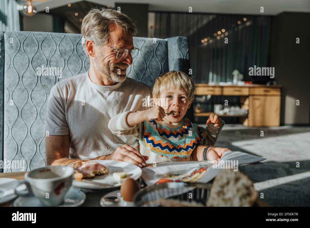 Junge, der am Tisch gegessen hat, während der Vater lächelte und im Hotel aussuchte Zimmer Stockfoto