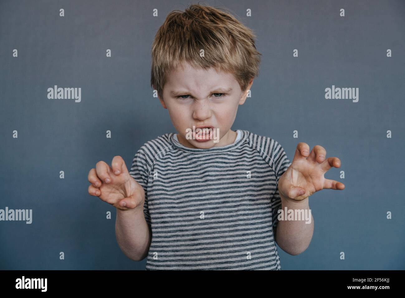 Wütender Junge, der gestikuliert, während er vor grauem Hintergrund steht Stockfoto