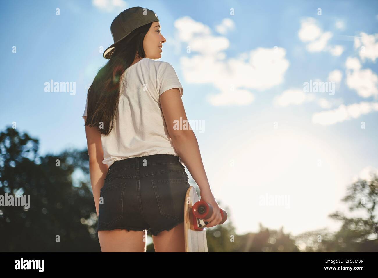 Urbaner Lifestyle, Sport und Jugendkonzept. Lower Angle Rückansicht schöne Frau in Shorts und Snapback hält Holz Penny Board, zur Seite drehen Stockfoto