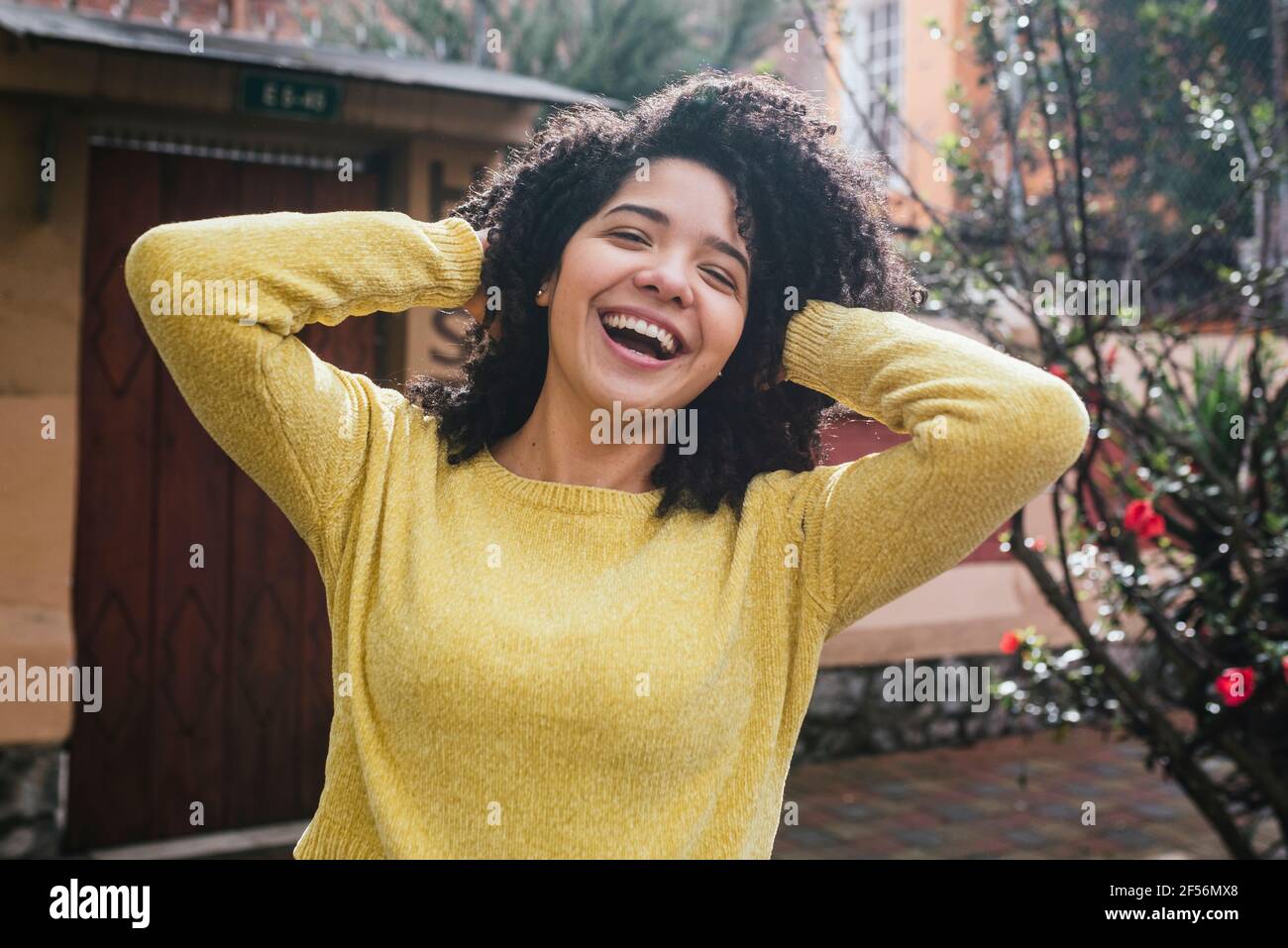 Fröhliche Frau in gelbem Pullover, die mit Haaren auf dem Rücken spielt Hof Stockfoto