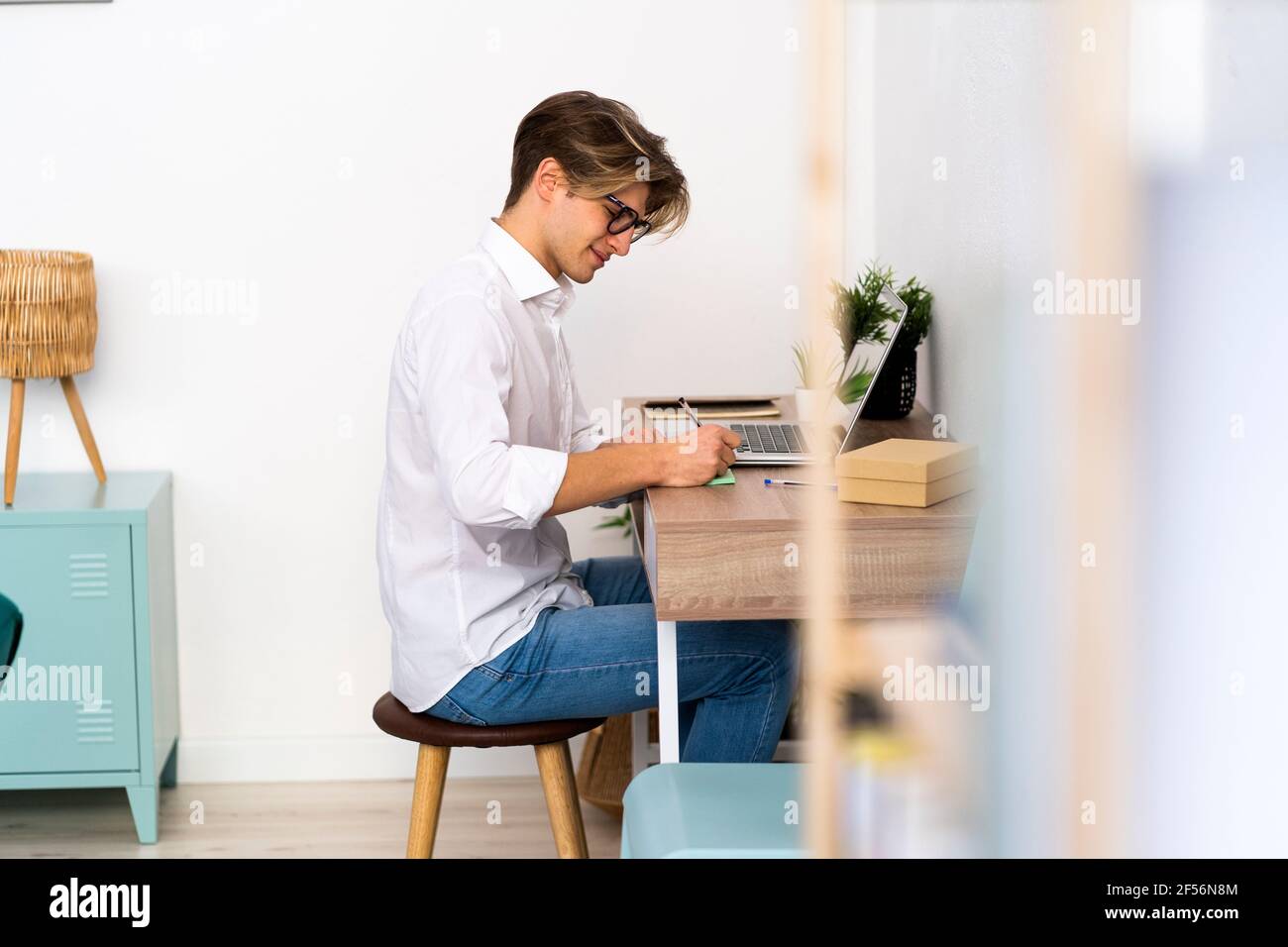 Junger Mann beim Schreiben am Tisch im Wohnzimmer Stockfoto