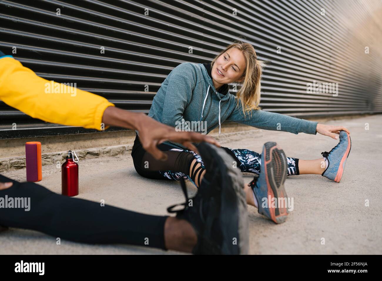 Lächelnde Sportlerin, die vom Sportler trainiert, während sie an der Wand sitzt Stockfoto