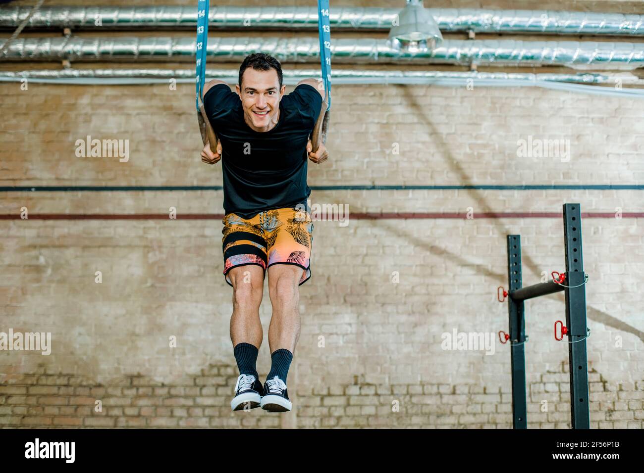 Lächelnder Mann, der im Fitnessstudio an Turnringen hing Stockfoto