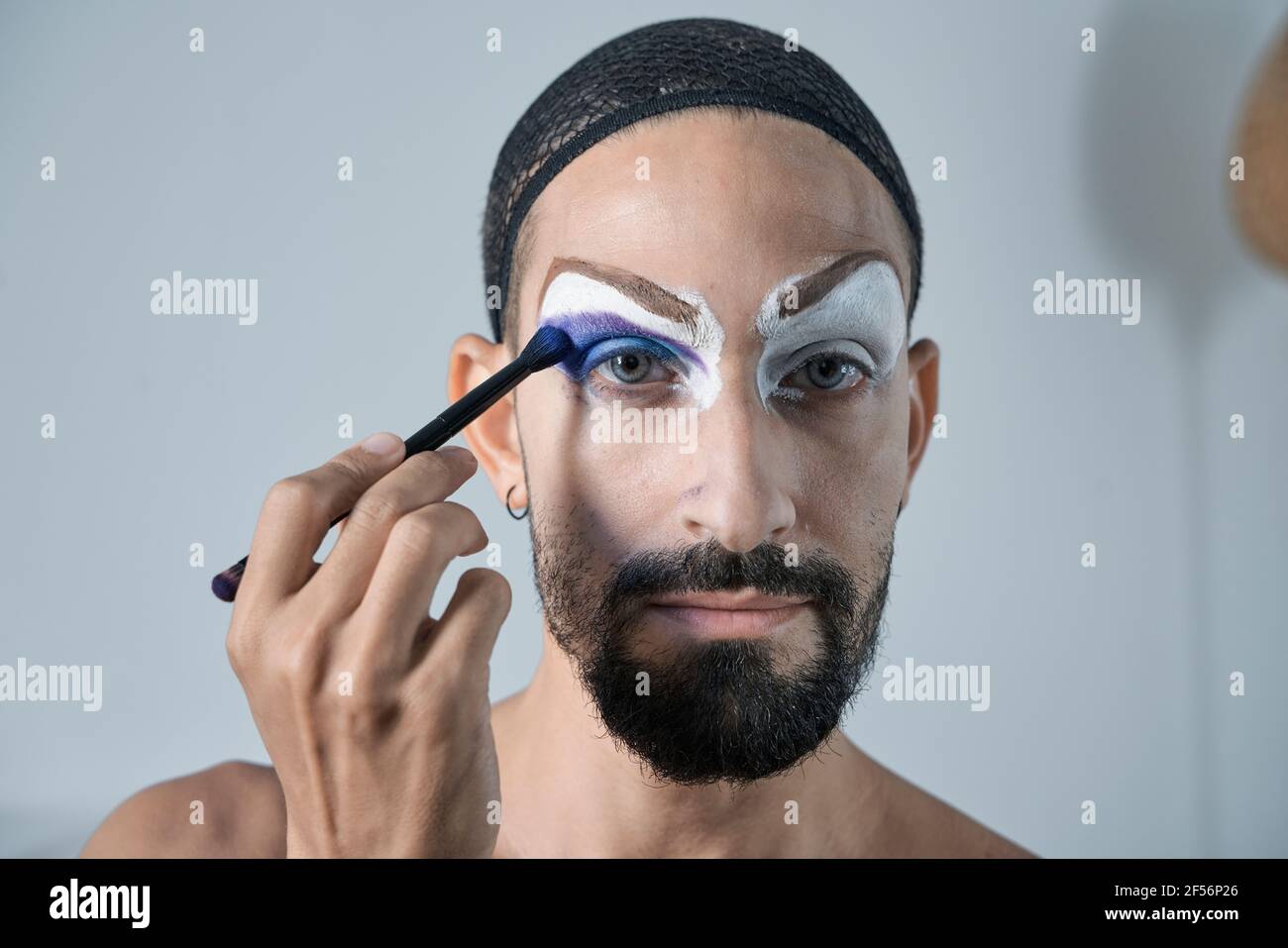 Mittelerwachsener Mann, der blauen Lidschatten mit Make-up-Pinsel aufführt Auge Stockfoto